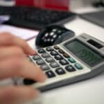 Dłoń przy biurku w biurze naciskająca klawisze kalkulatora