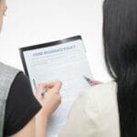 Dwie kobiety analizują wzór polisy ubezpieczeniowej przy biurku