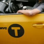 Kierowca żółtej taksówki w mieście opiera rękę o otwarte okno