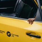 Pasażer otwiera drzwi żółtej taksówki z oznaczeniem stałej opłaty JFK