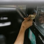 Pasażer płaci gotówką taksówkarzowi przez otwarte okno taxi
