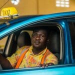 Taksówkarz z Ghany w kolorowej koszuli siedzi w niebieskiej taksówce