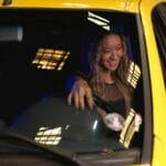 Uśmiechnięta kobieta prowadzi żółtą taksówkę nocą w mieście