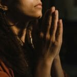 Zamyślona kobieta modląca się z złożonymi dłońmi w półmroku