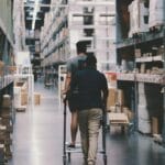 Dwaj pracownicy z wózkiem między regałami w dużej hurtowni logistycznej