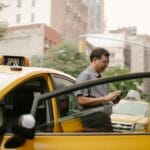 Mężczyzna w okularach przy taksówce sprawdza aplikację w telefonie