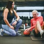 Starszy mężczyzna ćwiczy mięśnie brzucha z trenerem personalnym w siłowni