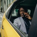 Zamyślony mężczyzna w garniturze rozmawia przez telefon na tylnym siedzeniu taxi