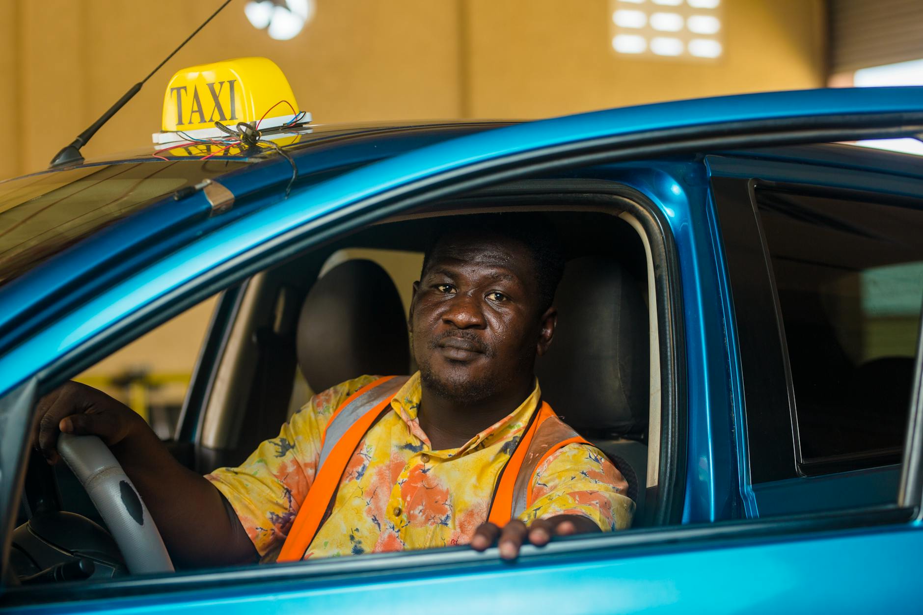 Kierowca taksówki w kolorowej koszuli siedzi w niebieskim aucie
