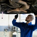 Mechanik w niebieskim kombinezonie sprawdza układ wydechowy samochodu