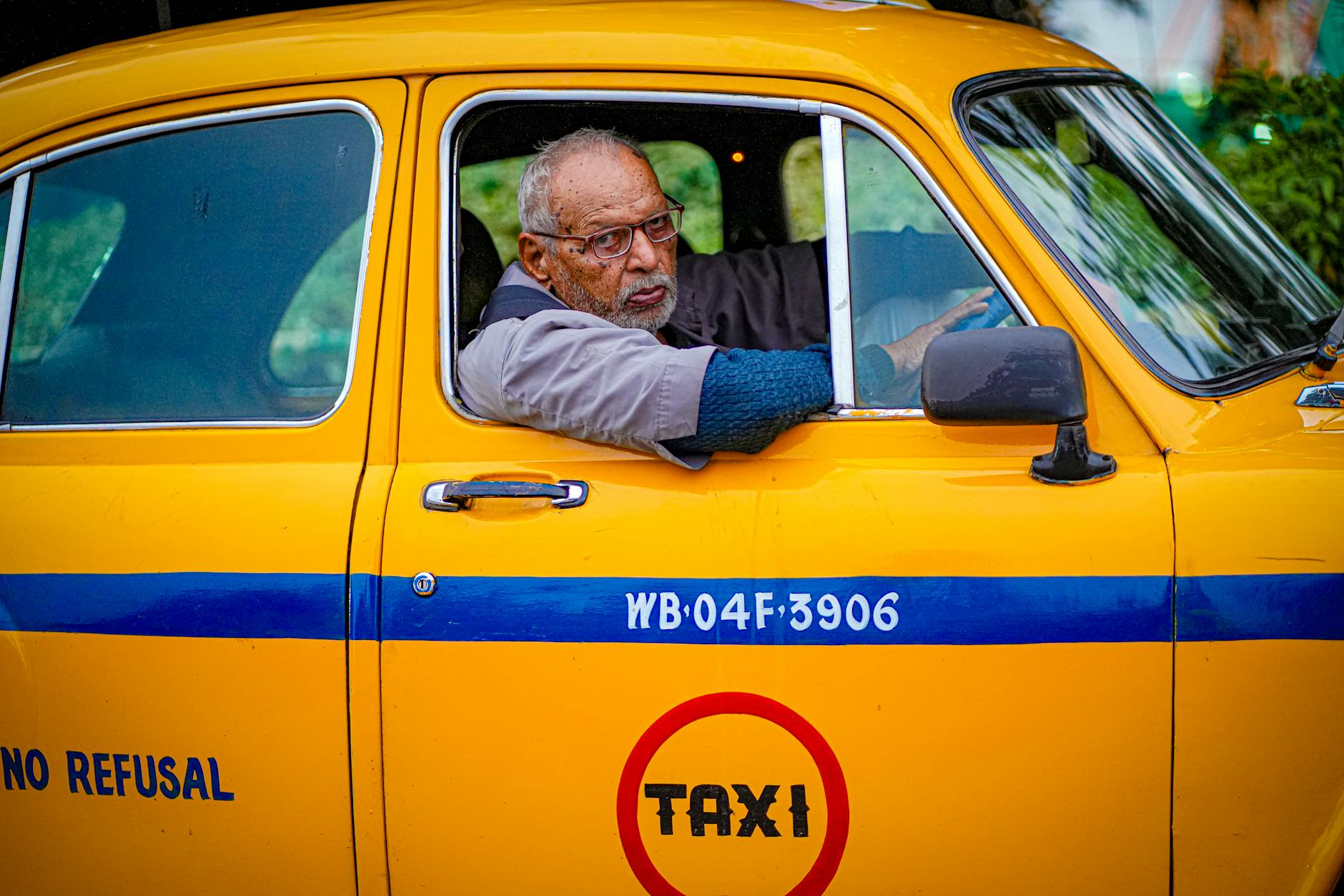Starszy kierowca prowadzi żółtą taksówkę na ulicy w Kolkacie