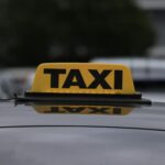 Żółty szyld taxi na dachu auta zaparkowanego w miejskiej strefie