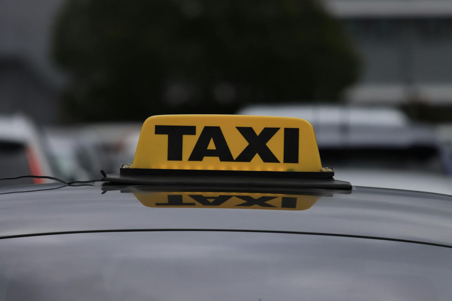 Żółty szyld taxi na dachu auta zaparkowanego w miejskiej strefie
