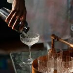 Domowy barman przelewający koktajl z shakera do szkła w przytulnym barze