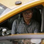 Azjatycki taksówkarz siedzi w mokrym aucie z otwartymi drzwiami
