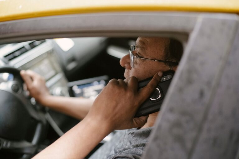 Mężczyzna w okularach rozmawia przez telefon za kierownicą żółtego auta